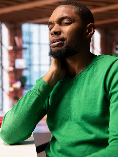 douleur-cervicale-homme-travail-bureau Homme souffrant de douleur chronique cervicale au travail, tenant son cou en position assise